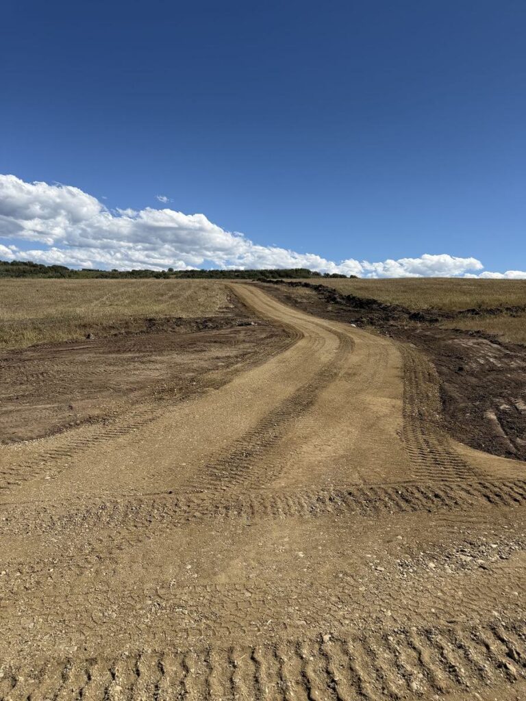 Gravel access road looking uphill after grading, shoulders cut back and the surface tracked in